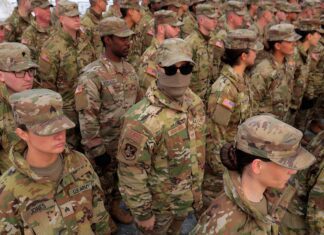 Pentágono avalia enviar mais 10 mil soldados ao Oriente Médio, diz jornal – 26/03/2026 – Mundo Grupo de soldados do Exército dos EUA em uniforme camuflado, alinhados em formação. Um soldado no centro usa óculos escuros e máscara facial, destacando-se entre os demais.