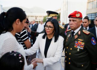 Venezuela: ex-chefe de espionagem vira ministro da Defesa – 26/03/2026 – Mundo Mulher de terno branco e óculos cumprimenta outra mulher vestindo blusa branca com bolinhas, em ambiente externo com outras pessoas ao fundo. Homem em uniforme militar com boina vermelha observa ao lado.
